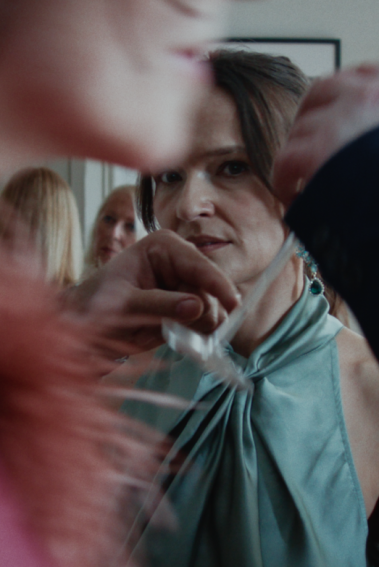 HÖFLICHE FÜNFZEHN MINUTEN Eine Frau steht inmitten eines Raums, um sie herum Menschen.