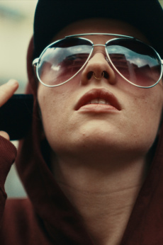 Eine Person mit Sonnenbrille und Kapuzenpullover hält sich das Handy ans Ohr.