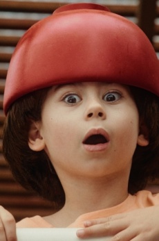 Ein Kind schaut erschrocken über ein Geländer. Es trägt eine rote Kopfbedeckung.