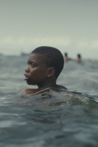 MAJINI Ein Junge schwimmt im Meer. Im Hintergrund ist ein Boot zu sehen.