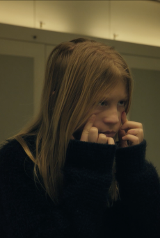 M. Ein Mädchen steht vorm Spiegel und hält sich im Gesicht.