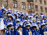 Eine Gruppe von Kindern und Erwachsenen in blau-weißen Kostümen steht dicht gedrängt vor der Rathausfassade.