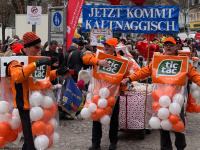 Faasenachtsumzug Dudweiler - Sonntag, 15. Februar 2026 Mehrere Männer in orangefarbenen Tic-Tac-Kostümen stehen mit einem Schild „Jetzt kommt kaltnaggisch“ vor einer großen Menschenmenge.