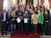 Eine Gruppe Menschen stehen auf einer Treppe und posieren für ein Foto. In der ersten Reihe in der Mitte halten ein Mann und eine Frau eine Urkunde in der Hand