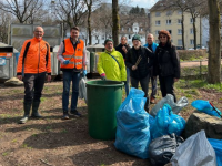 Gruppe von sieben Personen mit Müllsäcken und einer grünen Mülltonne im Freien 
