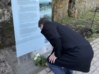 Ein Mann legt einen Blumenstrauß vor eine Infotafel