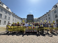 Personengruppe mit Bannern, Absperrbaken und gelben Schildern vor einem Gebäude mit Innenhof.