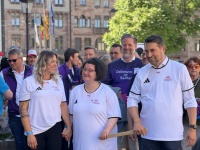 Personengruppe in weißen und violetten T-Shirts geht gemeinsam mit einer Laterne über einen Platz vor einem historischen Gebäude.