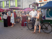 Menschen unterhalten sich auf einem Platz an Stehtischen. Eine Person steht mit einem Fahrrad im Vordergrund.