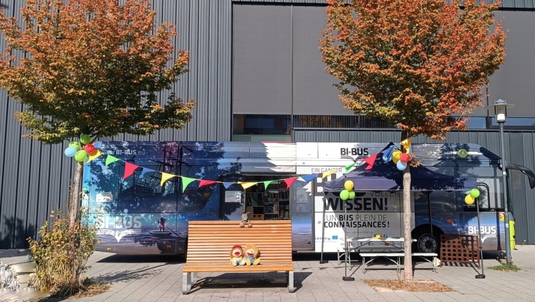Der Bücherbus auf dem Gelände des Eurobahnhofs, im Vordergrund zwei Bäume mit Herbstlaub