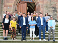 Gruppenfoto mit mehreren Personen auf einer Freitreppe vor einem historischen Gebäude mit geöffnetem Eingangsportal.