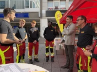 Mehrere Einsatzkräfte stehen mit einem Mann im Sakko im Gespräch an einem Informationsstand in der Fußgängerzone.
