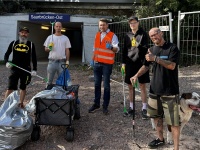 Fünf Männer mit Müllgreifern und Säcken stehen mit einem Hund vor dem Zugang zum Ostbahnhof.