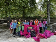 Erwachsene und Kinder in bunten Warnwesten stehen mit gesammelten Müllsäcken und einem World-Cleanup-Day-Banner im Park.