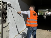 Oberbürgermeister Uwe Conradt streicht in Warnweste eine mit Graffiti besprühte Wand einer Unterführung.
