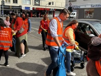 Oberbürgermeister Uwe Conradt sammelt mit mehreren Personen in Warnwesten Müll auf einem Gehweg.